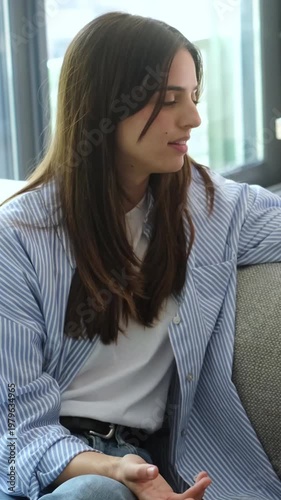 Thoughtful Young Woman Engaged in Conversation while Sitting Comfortably on a Sofa Indoors
