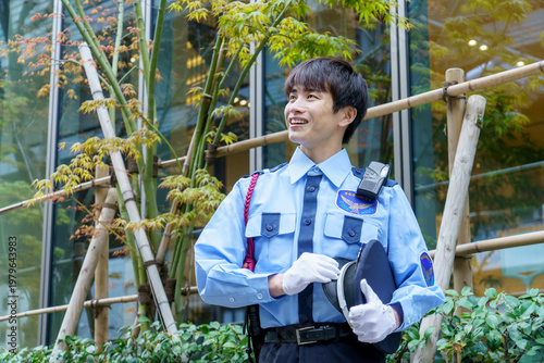 オフィスビルの前に立つ若い日本人男性警備員　撮影協力：学校法人電波学園　東京電子専門学校