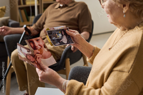 Senior woman holding family photos and discussing memories during support session, representing aging, reminiscence, dementia care. Useful for healthcare, senior living, caregiving campaigns