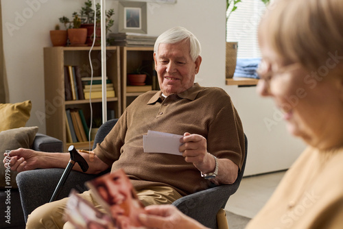 Fotografia Senior Caucasian man holding family photo and smiling while sitting with senior woman, recalling memories and bonding at home