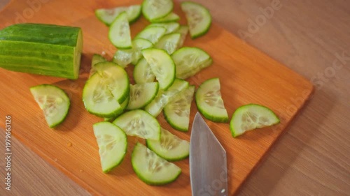 Chef's skilled hands carefully place sliced fresh green cucumber on rustic cut wooden board, showcasing chopping process. vegetable lies perfectly arranged, demonstrating precise culinary techniques