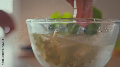 A housewife gently washes fresh herbs in a bowl of water, rinsing the greens before assembling a crisp salad. The careful cleaning ensures vibrant flavor and food safety in the kitchen
