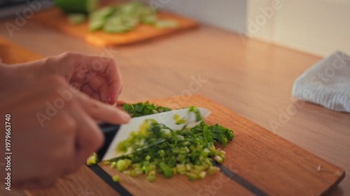 Kitchen knife swiftly chops fresh greens on a wooden cutting board, as a housewife's skilled hands prepare ingredients for a healthy salad, showcasing her cooking expertise in a home kitchen setting
