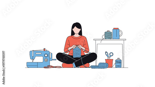Woman sitting on the floor knitting a blue scarf with a sewing machine and colorful thread spools on a table in her home crafting studio.
