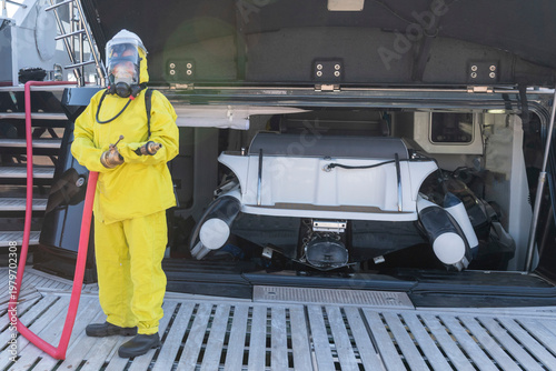 Fire drill on yacht stern: crew member in protective suit uses fire hose and breathing apparatus during training, simulating emergency firefighting on board.