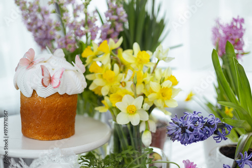 Easter cake with white icing and butterfly decoration surrounded by spring flowers, bright festive composition with copy space on light background.