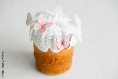 Easter cake with white icing and delicate pink butterfly decorations on light background. Minimal festive dessert concept with soft pastel tones and copy space.
