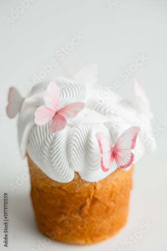 Easter cake with white icing and delicate pink butterfly decorations on light background. Minimal festive dessert concept with soft pastel tones and copy space.