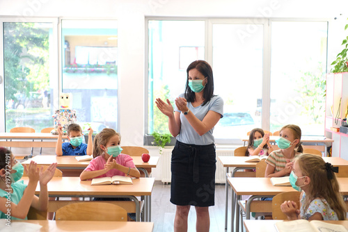 Teacher and elementary students wearing masks in classroom clapping and celebrating safe return to school