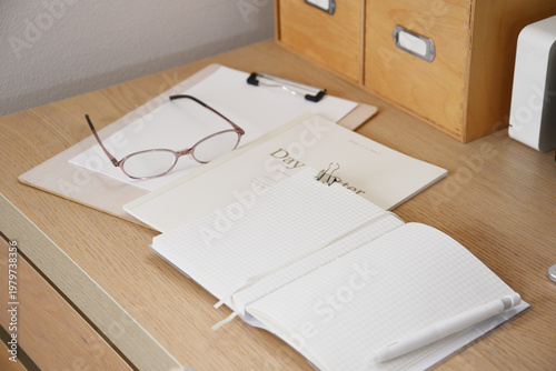 Glasses notebook and clipboard arranged on clean wooden desk