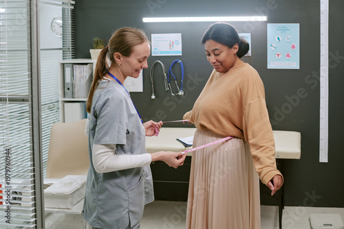 Foto Caucasian female clinician measuring pregnant Black woman waist during prenatal