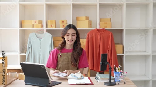 A small startup business run by a young Asian woman working from home, using a laptop for online marketing and preparing packaging for customer orders.