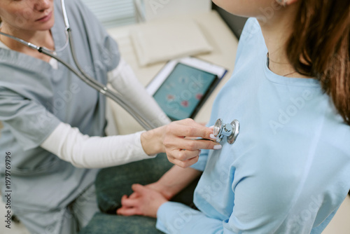Tableau sur toile Close up of middle aged female doctor examining young adult woman with stethosco