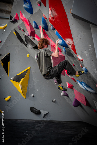 portrait shot of young white slim indoor rock climber om overhang with flexed arms and cut loose feet on bouldering wall