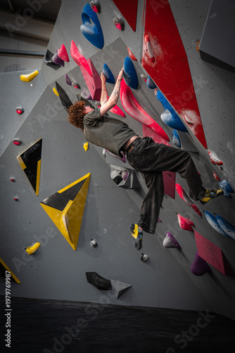 portrait shot of young white slim indoor rock climber om overhang with flexed arms and cut loose feet on bouldering wall