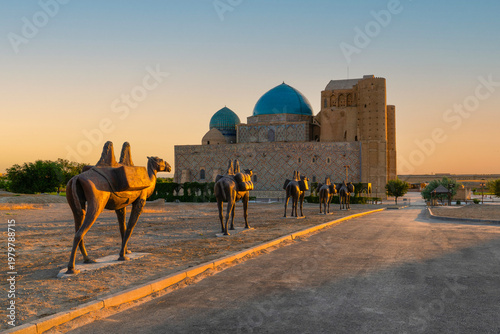 Turkestan, Kazakhstan - June 03, 2025: Scenic early morning sunrise view of the historical Mausoleum of Khoja Ahmed Yasawi (Қожа Ахмет Ясауи) with a bronze camel statue in the foreground