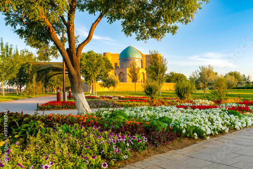 Turkestan, Kazakhstan - June 03, 2025: Scenic early morning sunrise view of the historical Rabia Sultan Begim Mausoleum framed by a park pathway and vibrant spring flowers