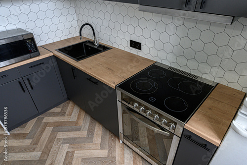 Tableau sur toile A modern kitchen with a black sink, wooden countertop, induction stove, dark cabinets, hexagonal tile backsplash and herringbone wooden floor