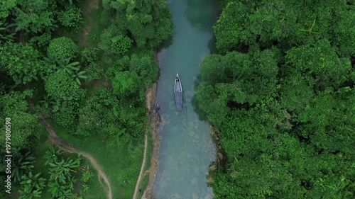 Boat sailing through clear river in lush green forest.