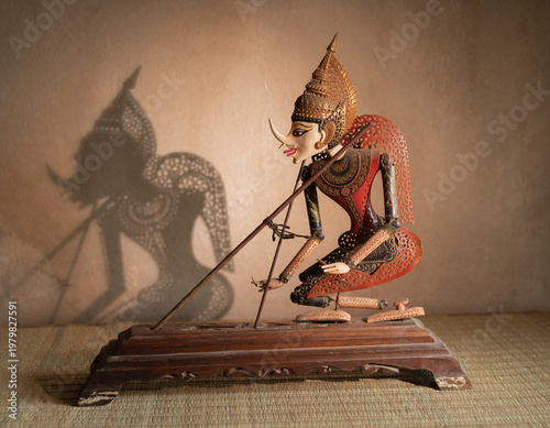 Single Wayang Kulit Shadow Puppet on Traditional Wooden Stand with Dramatic Shadow Cast on Textured Wall, Indonesian Heritage Art and Cultural Craft
