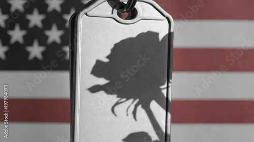 Close up of military dog tags with a rose shadow against blurred American flag background for Memorial Day veteran remembrance and tribute