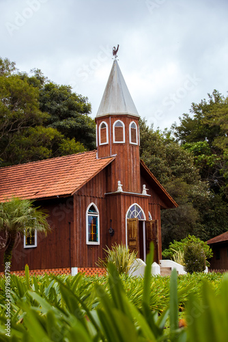 Foto Small rustic wooden church with terracotta roof and weathercock surrounded by lu