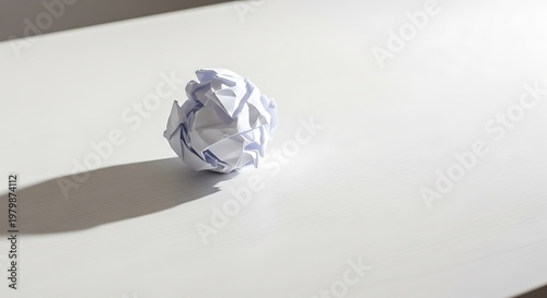 A crumpled piece of paper casting a shadow on a white surface, representing ideas, creativity, and mistakes