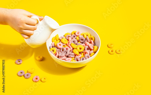 Fotografía A child’s hand pouring milk into colorful fruity cereal loops
