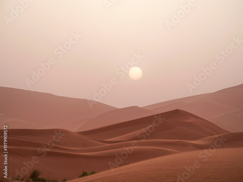 Minimalist pale sun low on horizon above curved sand dunes at sunset Merzouga Sahara