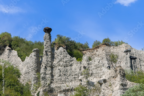 Jagged white cliffs of Pyramids of Zone fill mountainside, dark boulder crowns highest earth column while smaller hoodoos and sparse vegetation spread across bright mineral slope