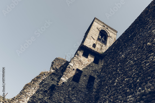 Bell tower and massive defensive wall of old castle in Cavriana Lombardy Italy, angled frame and analog film effect emphasize rugged masonry stark light muted tones