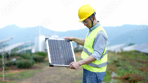 Photography Engineer inspecting a handheld solar panel on-site at a mountainous photovoltaic