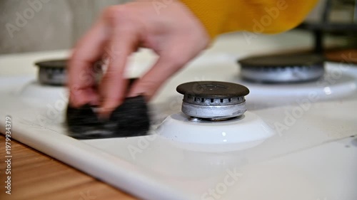 Hand scrubbing gas stove surface with cleaning brush in modern kitchen setting