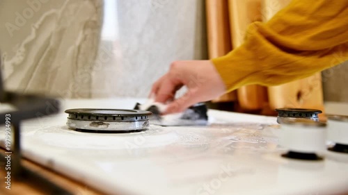 Hand cleaning gas stove surface with sponge in modern kitchen setting
