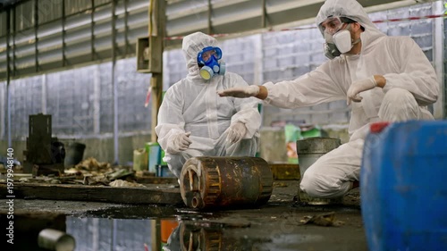 Hazardous waste chemical spill industrial site, hazmat worker protective suit respirator, contamination cleanup operation, toxic pollution control as workers inspect equipment and handle industrial