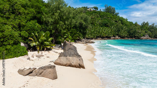 A sandy beach with rocks and lush green vegetation, bordered by clear turquoise waters. Seychelles, Mahe. Anse Intendance.