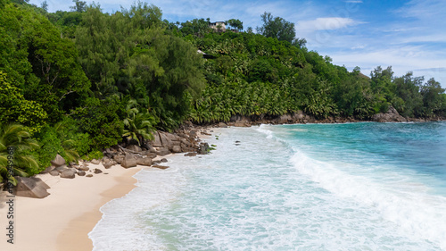 A secluded tropical beach with large rocks and lush palm trees, turquoise waters lapping the shore. Anse Intendance. Seychelles, Mahe.