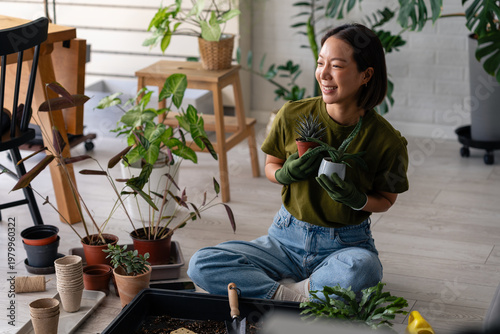 Photography Smiling young Asian woman sitting on the floor repotting houseplants, holding su