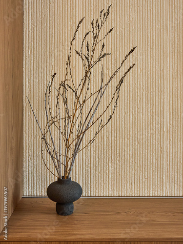 Minimalist interior with dried branches in a dark textured vase on a wooden shelf. Beige ribbed wall background. Japandi style home decor.