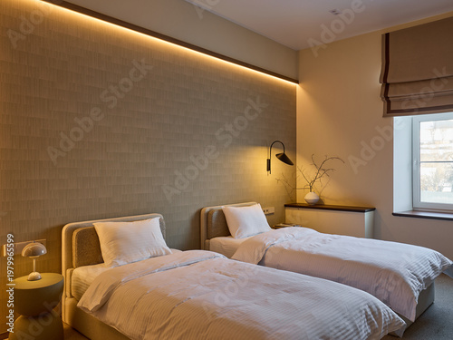 Modern hotel room interior with twin beds, white linens, and a long upholstered headboard. Wooden log side table, lamps, and beige curtains. Minimalist design.