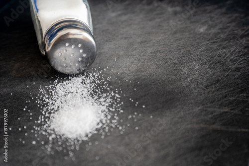 Photos Glass Salt Shaker on Its Side with Salt Pile on Dark Slate