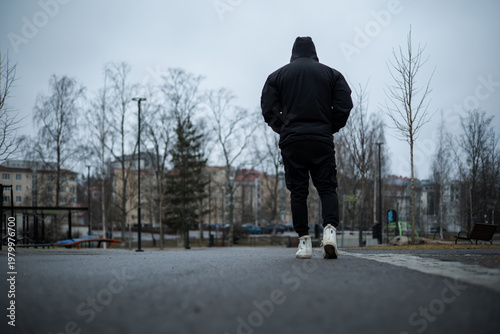 Quadro su tela Hooded Man Walking Away in Overcast Urban Park
