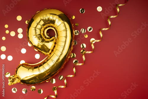 9th birthday celebration. Gold festive balloons number 9 year anniversary on red background with confetti. Birthday or wedding event.