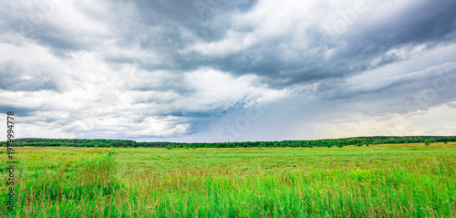 Fotografie Vast green field stretches under heavy, brooding clouds