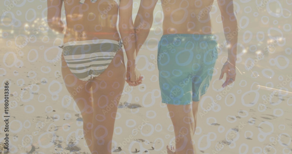 Fototapeta premium Walking couple holding hands on beach with striped bikini bottoms, aqua trunks, footprints, overlay