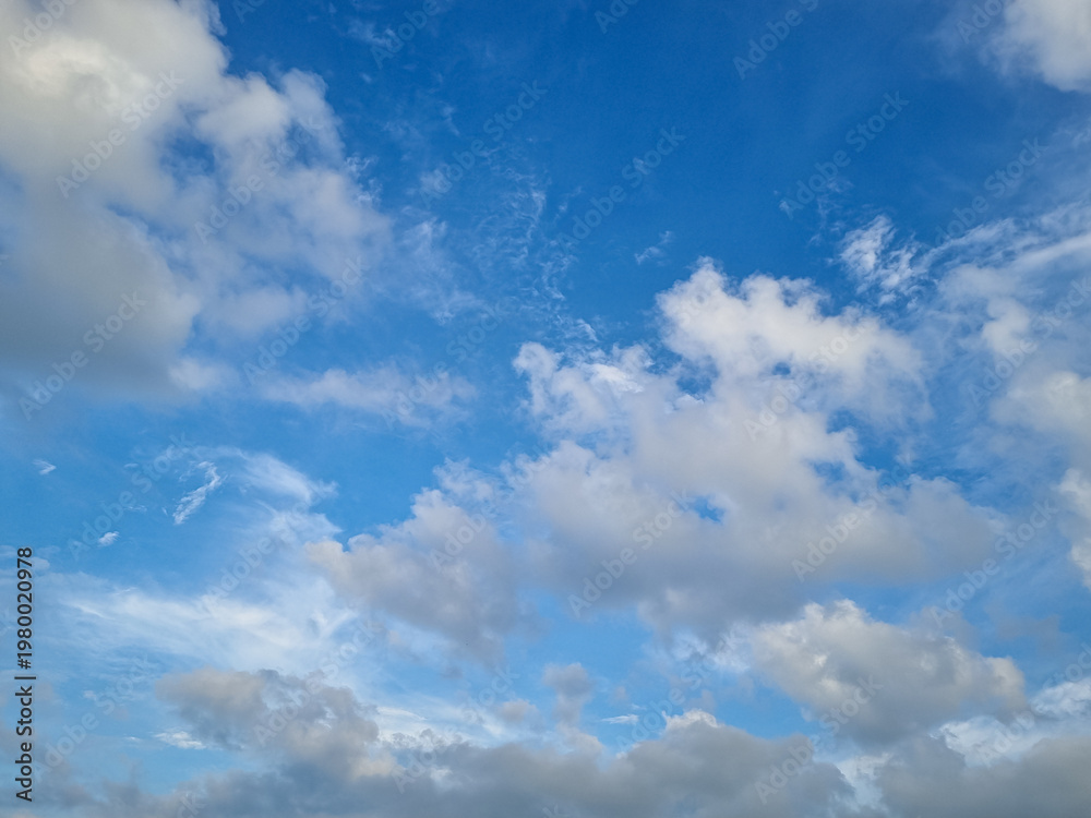 Fototapeta premium Bright blue sky filled with soft scattered white clouds creating peaceful natural atmospheric background scene