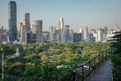 The view of the Bangkok skyline from Lumpini Park shows a lush green urban landscape and modern skyscrapers, including a bridge in Dusit Central Park, Bangkok, Thailand.