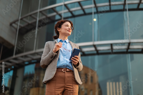 Foto Businesswoman holding smartphone with confident gaze reflecting determination