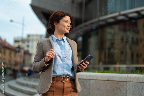 Fotografía Businesswoman holding smartphone in city looking ahead