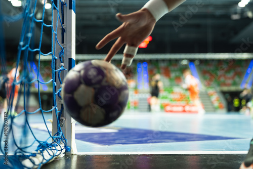 Fotografie A handball goalkeeper's hand with athletic tape reaching for a ball near the goal post during an intense moment of the game